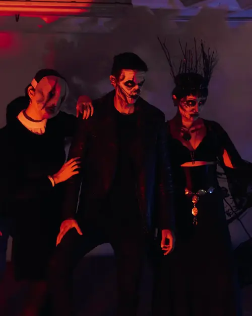 Drei Freunde mit Horror-Make-up und dunklen Kostümen in rotem Licht und Nebel auf einer Halloween-Party Drei Freunde mit Horror-Make-up und dunklen Kostümen in rotem Licht und Nebel auf einer Halloween-Party