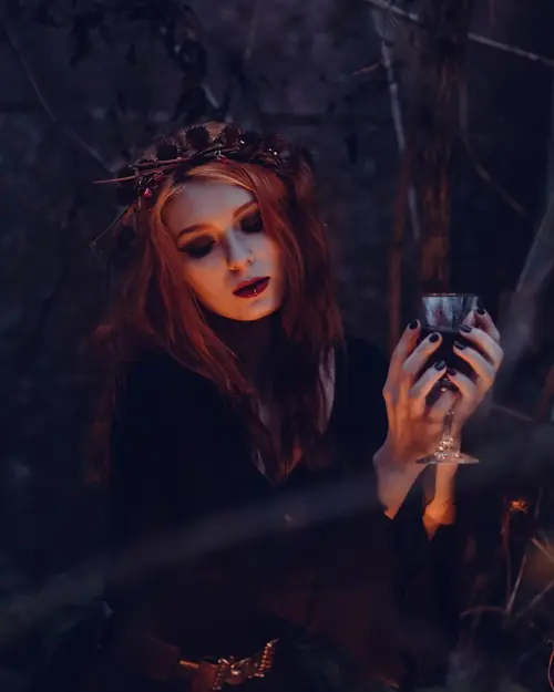 Frau als Hexe verkleidet hält nachts im dunklen Wald einen Kelch Frau als Hexe verkleidet hält nachts im dunklen Wald einen Kelch