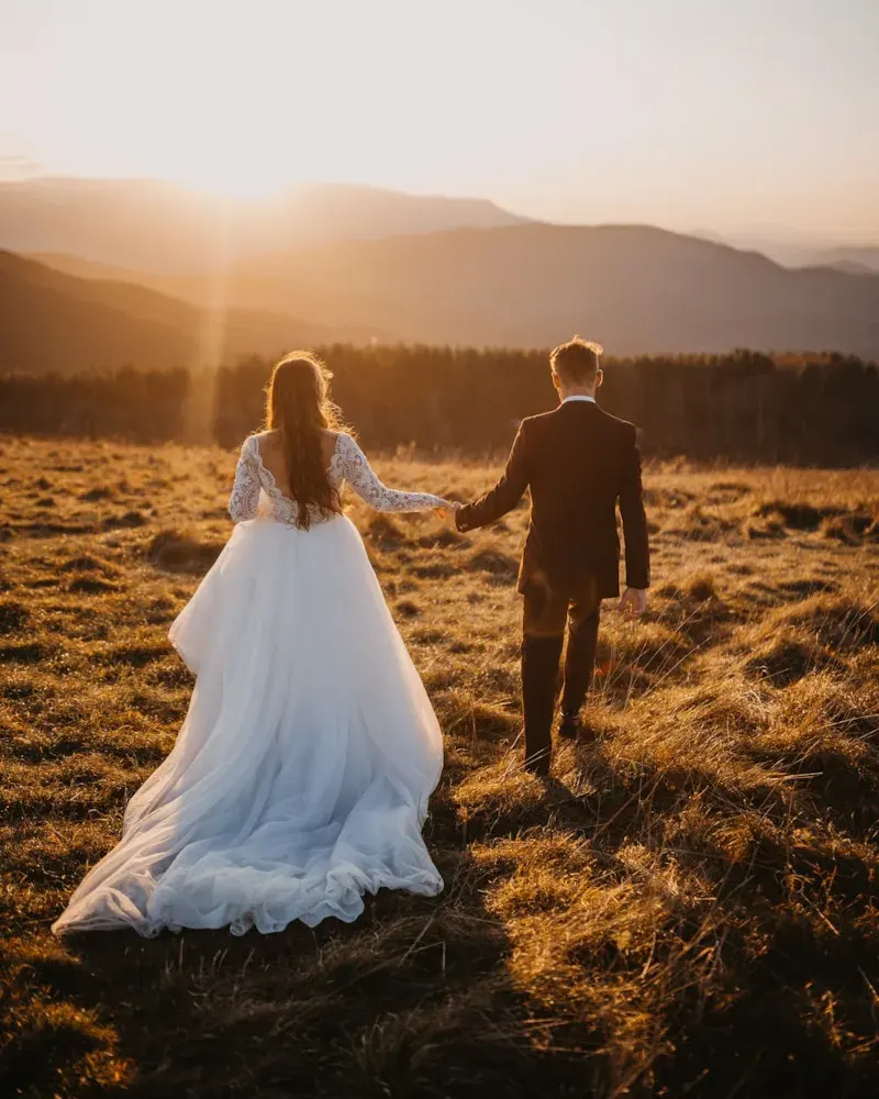 A couple walking hand in hand through a field at sunset