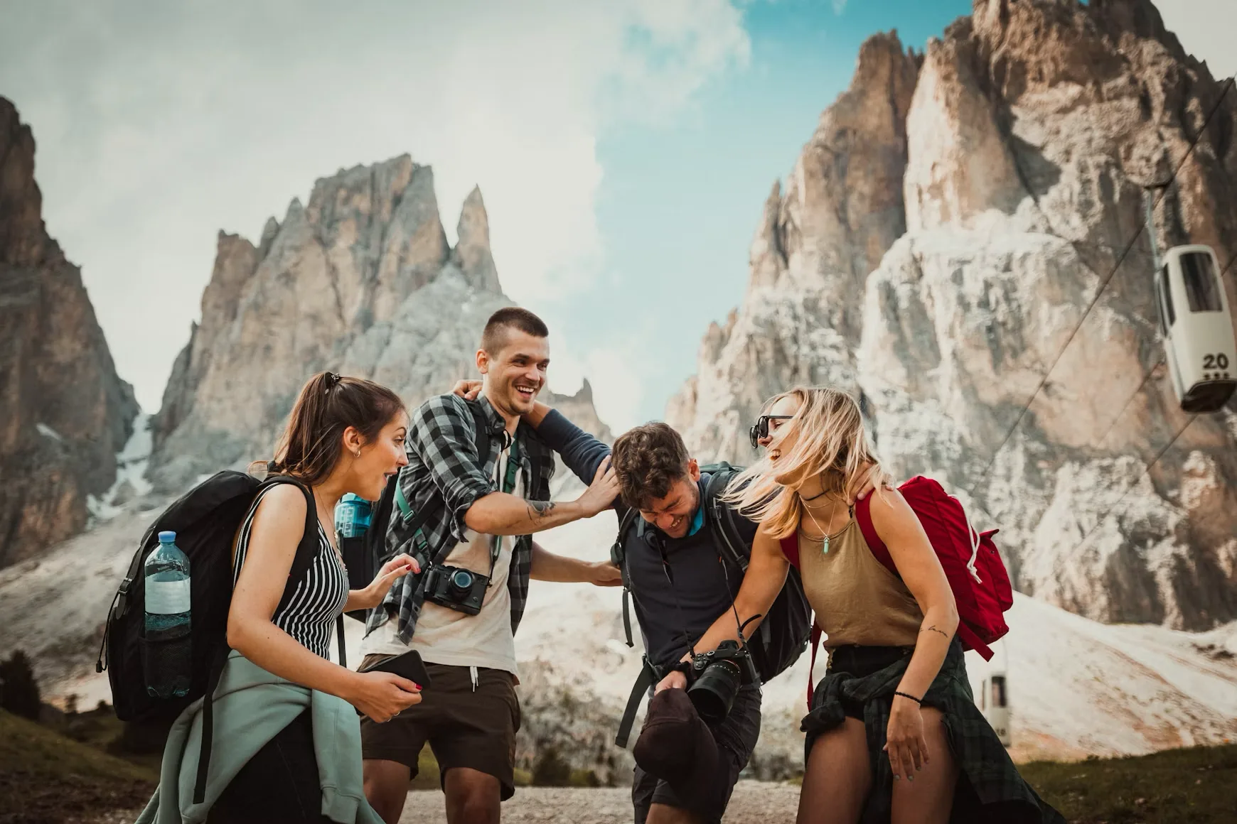 Four friends with backpacks and cameras laughing together on a mountain trail in the Dolomites